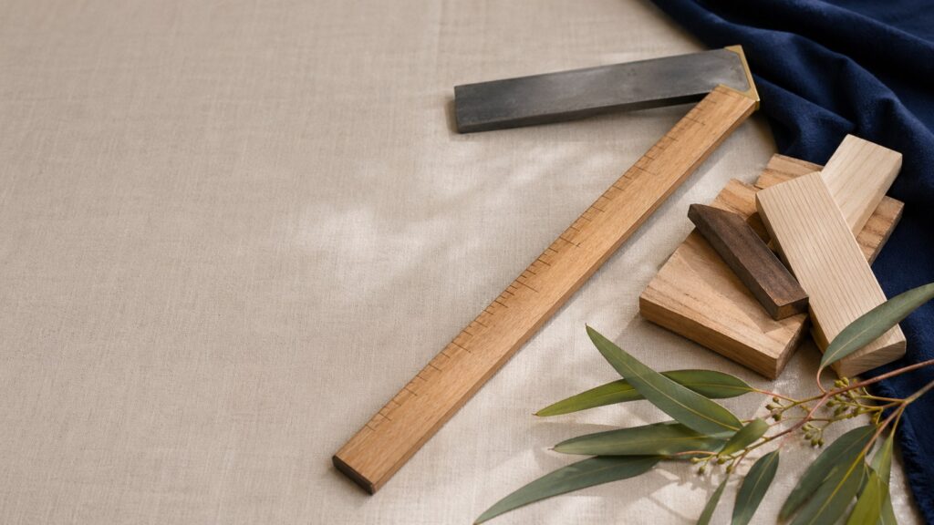 A small timber offcut, tool and folded papers arranged on a light cloth.