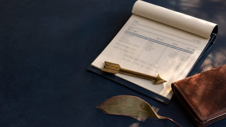 A clipboard, wallet and folded leaf beside a pen on navy fabric.