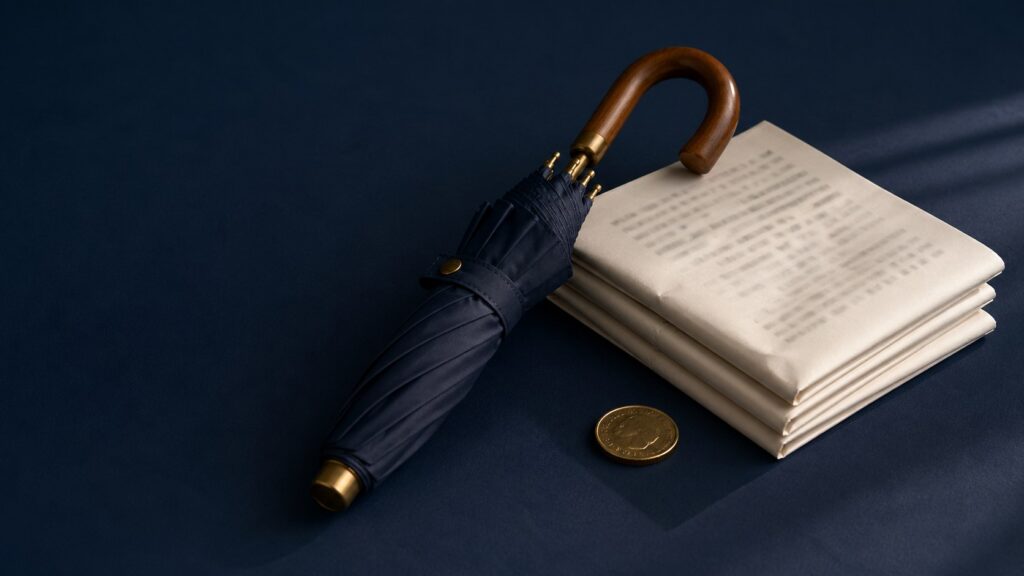 A navy umbrella beside folded papers and a coin on dark blue cloth.