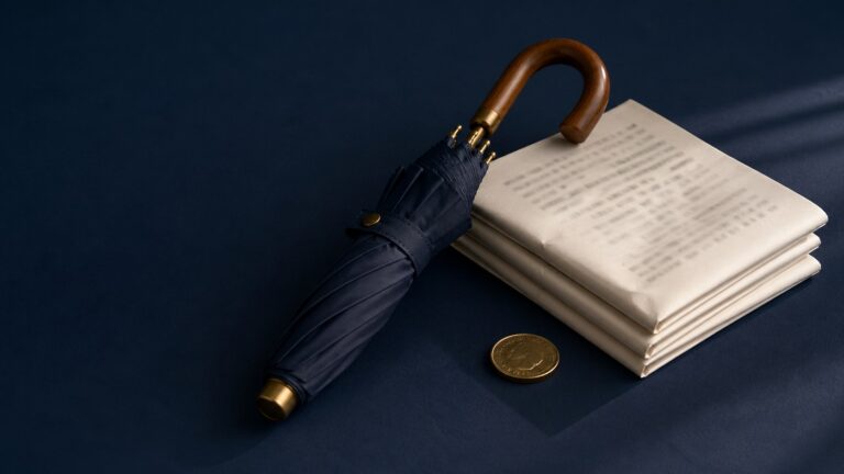 A navy umbrella beside folded papers and a coin on dark blue cloth.