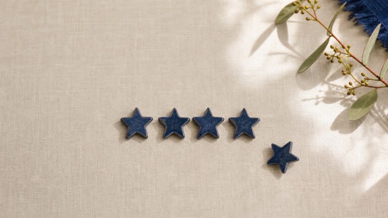 Five small blue rating stars laid on linen beside a gum branch.